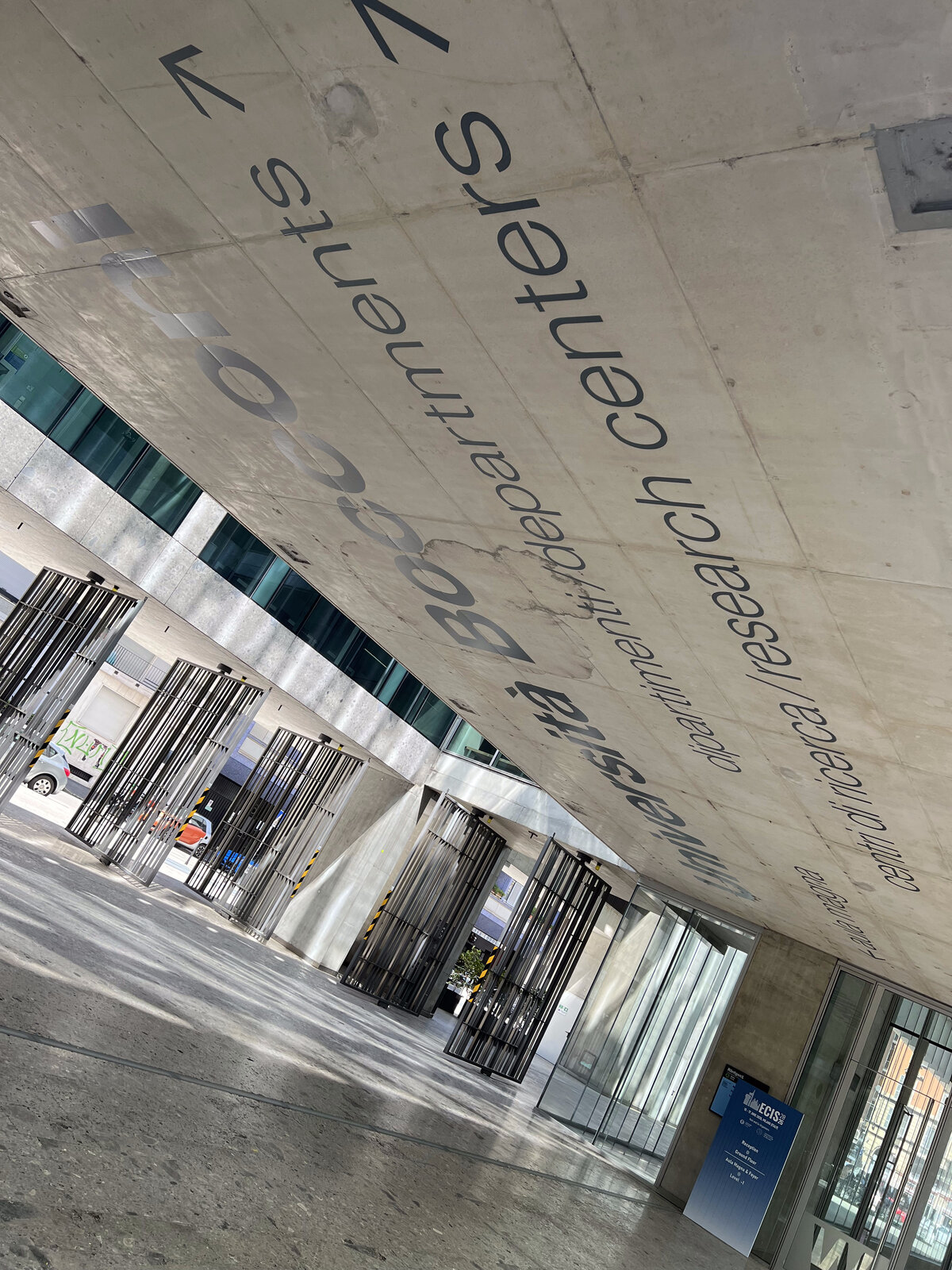 Courtyard of Bocconi's SANAA campus, under the canopy with the university's departments and research centers written on the ceiling